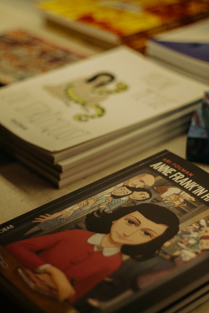 A close-up of a stack of books featuring a graphic novel of Anne Frank, indoors.